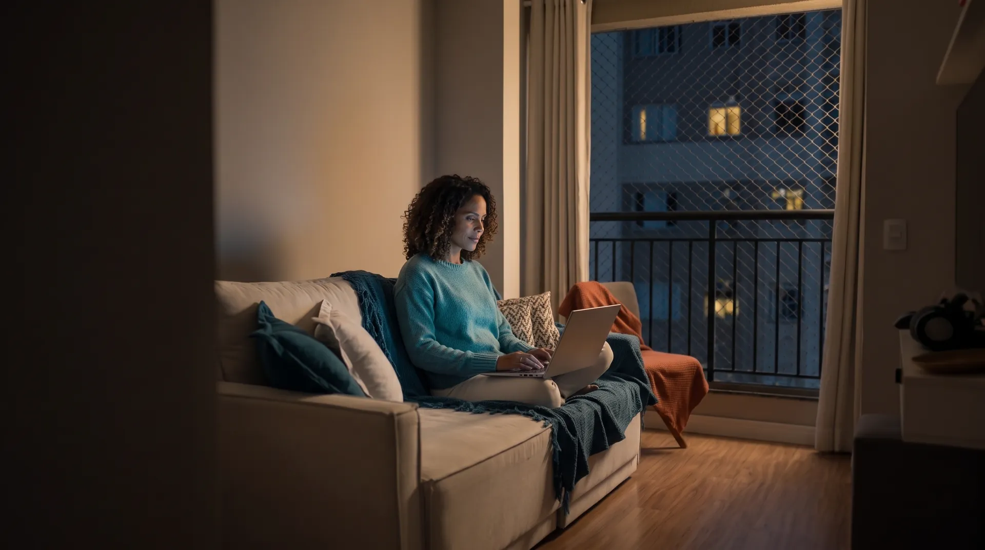 Moradora no sofá de casa, à noite, com o notebook